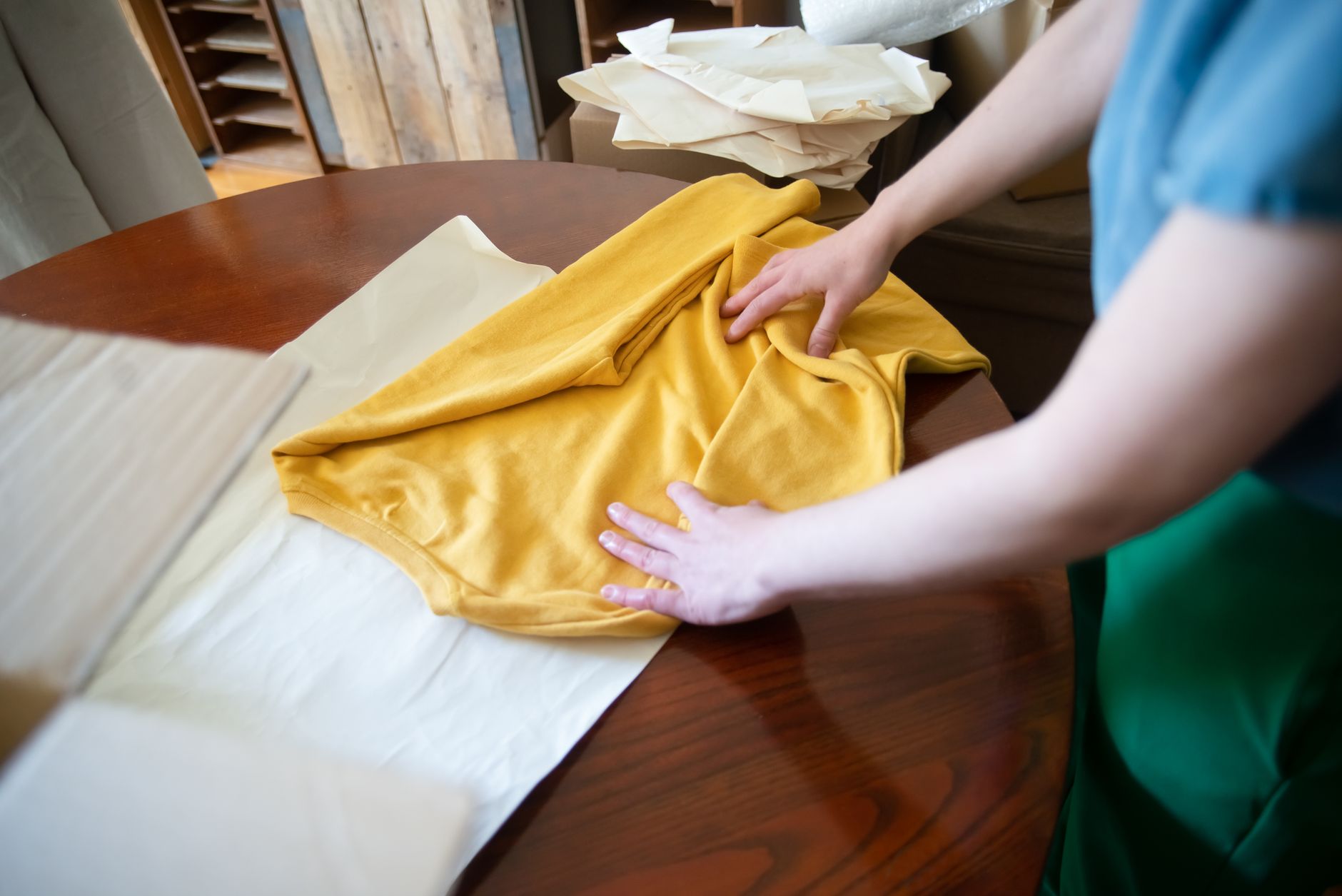 a person folding a yellow shirt on a wooden table